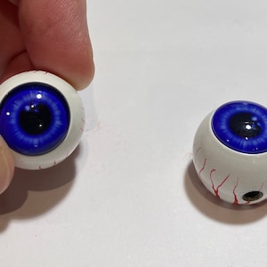 May include: Two blue eyeball-shaped ornaments with red veins. The eyeballs are white with a blue iris and black pupil.