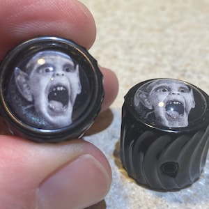 May include: Two black guitar knobs with a white and black image of a screaming face.