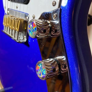 May include: Close-up of a blue electric guitar with chrome knobs. The knobs have a swirling iridescent design.
