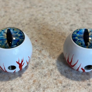 May include: Two white round knobs with a blue eye design and red flames painted on the bottom.