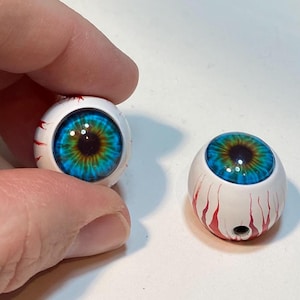 May include: Two blue and green eyeball-shaped ornaments with white and red paint. The ornaments are about 2 inches in diameter.