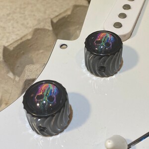 May include: Two black guitar knobs with a rainbow skull design. The knobs have a textured, spiral pattern.