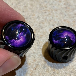 May include: Two black guitar knobs with a purple and black galaxy design.