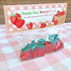 Könnte beinhalten: Ein durchsichtiger Plastikbeutel gefüllt mit erdbeerförmigen Bonbons, versehen mit einer rechteckigen Karte mit rosa-weißem Vichy-Muster, roten Erdbeerillustrationen und dem Text Thank You BerryMuch For celebrating my 6th birthday with me! Love, Quinn.