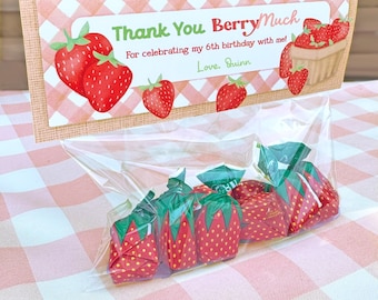 May include: A clear plastic treat bag filled with strawberry-shaped candies, topped with a rectangular card featuring a pink and white gingham pattern, red strawberry illustrations, and the text Thank You BerryMuch For celebrating my 6th birthday with me! Love, Quinn.
