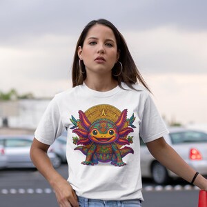 May include: White t-shirt featuring a colorful axolotl design with a sun-like background. The axolotl has intricate patterns and vibrant colors. The shirt also has the text "IKACHI ART Love for Our Roots" in the upper left corner.