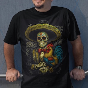 Puede incluir: Camiseta negra con un diseño del Día de Muertos. El gráfico incluye un esqueleto con sombrero y traje, sosteniendo un gallo. El diseño es colorido con detalles dorados, rojos y azules.