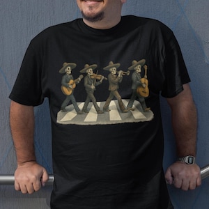 May include: Black t-shirt featuring a humorous illustration of four skeleton mariachi musicians crossing a street, each playing a different instrument. The image is a parody of the iconic Abbey Road album cover.