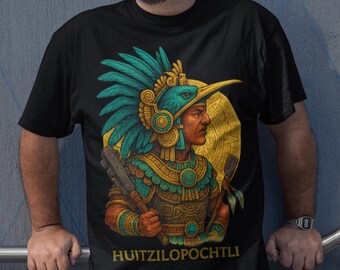 May include: Black t-shirt featuring a detailed illustration of a figure in traditional Aztec attire, including a feathered headdress and ornate clothing. The text "HUITZILOPOCHTLI" is printed below the image. The person is smiling.