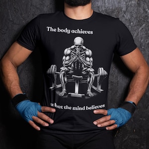 Puede incluir: Camiseta negra con un gráfico de un esqueleto sentado en un banco de pesas, con el texto "The body achieves what the mind believes". La persona lleva vendas azules en las manos.