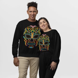 May include: Two black sweatshirts with a colorful luchador mask design. The mask is outlined in yellow and has blue, red, and green details.