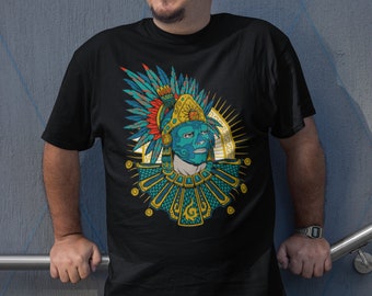 Puede incluir: Camiseta negra con una ilustración detallada de un guerrero azteca. El diseño presenta una cara turquesa, un elaborado tocado y detalles dorados. El diseño incluye plumas rojas, azules y amarillas. La camiseta tiene cuello redondo.