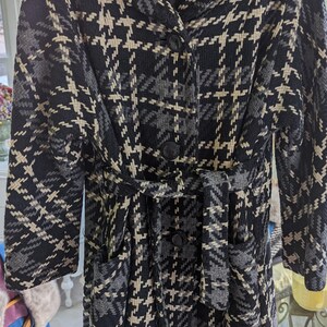 May include: A black and white houndstooth patterned coat with a belt and pockets. The coat has a collar and buttons.
