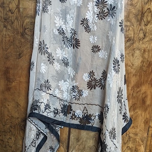 May include: A sheer scarf with a black and white floral pattern. The scarf is made of a lightweight fabric and has a fringed edge.