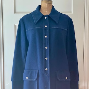 May include: A navy blue vintage coat with a collared neckline, long sleeves, and two front pockets. The coat features white stitching and silver buttons down the front. The coat is displayed on a mannequin.
