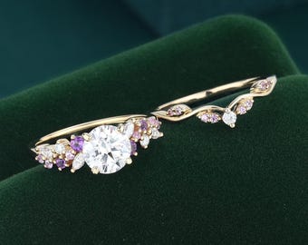 May include: A gold ring set featuring a central round white stone flanked by clusters of small purple and white stones, accompanied by a matching curved band adorned with a series of small pink stones arranged in a leaf-like pattern along the band.
