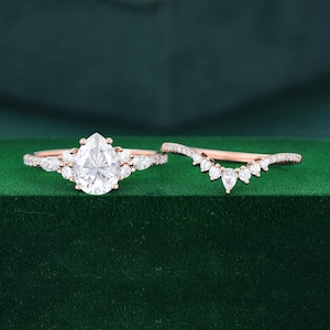 May include: A rose gold engagement ring set featuring a central pear-cut stone flanked by smaller pear and round stones on the band, accompanied by a matching curved wedding band set with a series of small round stones along the top edge.