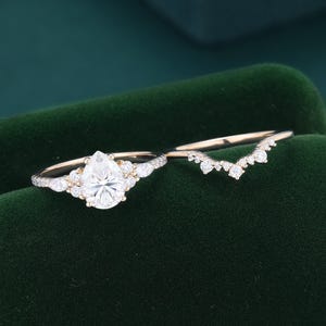 May include: A gold ring set consisting of a pear-cut center stone flanked by smaller round and marquise-cut stones, paired with a matching chevron-shaped band featuring a row of small round stones along the top edge of the band.