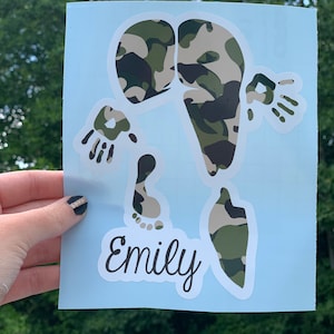 May include: A light blue background with a white outline of a person's body with handprints and footprints. The body is filled with a camouflage pattern in shades of green and brown. The name "Emily" is written in black cursive below the body.