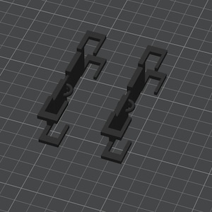 Puede incluir: Dos objetos negros, geométricos, renderizados en 3D, con un diseño en forma de gancho. Cada objeto tiene una serie de bloques rectangulares conectados por pequeños anillos circulares. Los objetos están sobre un fondo de cuadrícula gris oscuro.