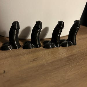 May include: Four small, black, 3D printed objects in a row on a wooden surface.