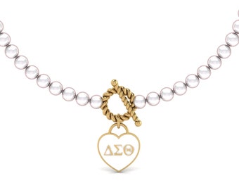 Op de afbeelding: Een parelketting met een goudkleurige toggle sluiting en een hartvormige hanger. De hanger toont de Griekse letters ΔΣΘ in goud.