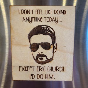 May include: Wooden plaque with a burned image of a man wearing sunglasses and a beard. The text reads, "I DON'T FEEL LIKE DOING ANYTHING TODAY... EXCEPT ERIC CHURCH. I'D DO HIM."