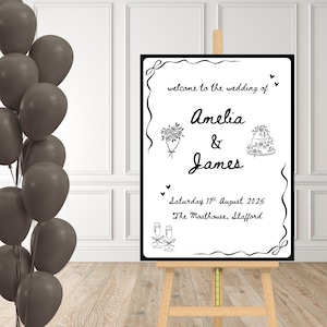 May include: A wedding sign in black and white on a wooden easel. The sign says "welcome to the wedding of Amelia & James" with the date and location. Illustrations of a bouquet, cake, and champagne glasses are included. A bunch of grey balloons is on the left.