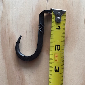 May include: A black metal hook measuring 3 inches in length. The hook is bent into a J shape and has a twisted design. The hook is next to a yellow measuring tape.