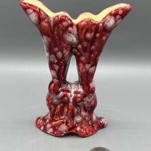 May include: A unique, red and white ceramic vase with a distinctive shape. The vase has a flared top with a yellow interior and a textured, mottled surface. The base is bulbous and the overall design is artistic and eye-catching.