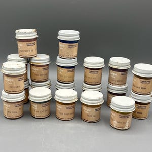 May include: A collection of small glass jars with white lids, labeled with various colors and the brand "Unique Colors." The jars contain translucent underglaze paints, with labels indicating specific shades like "Deep Red" and "Coral."