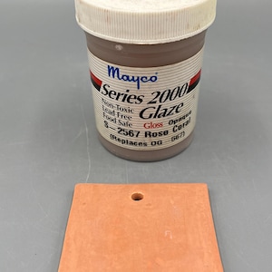 May include: A jar of Mayco Series 2000 Rose Coral glaze with a matching ceramic tile. The glaze is non-toxic, lead-free, and food safe. The tile is a square shape with a hole at the top, and is a coral color.
