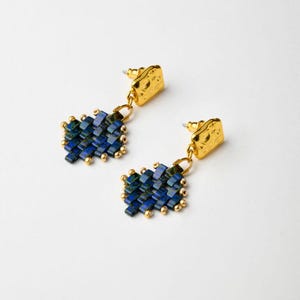 Op de afbeelding: Een paar gouden oorhangers met blauwe en groene geometrische kralenclusters.