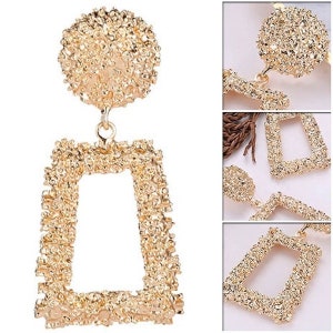 May include: Gold-tone statement earrings with a textured, geometric design. The earrings feature a large, round top piece and a rectangular bottom piece.