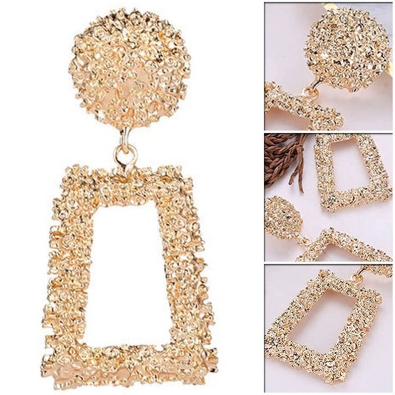 May include: Gold-tone statement earrings with a textured, geometric design. The earrings feature a large, round top piece and a rectangular bottom piece.