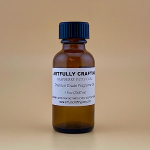 May include: A brown glass bottle with a black cap, labeled "ARTFULLY CRAFTING RASPBERRY PATCHOULI Premium Grade Fragrance Oil 1 fl oz (29.57 ml)" and "www.artfullycrafting.etsy.com".