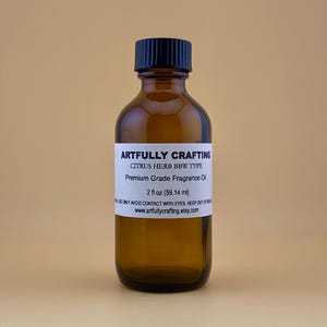 May include: A brown glass bottle with a black cap, labeled "Artfully Crafting" and containing "Citrus Herb BBW Type Premium Grade Fragrance Oil" in a white label. The bottle contains 2 fl oz (59.14 ml) of fragrance oil.