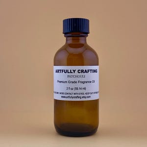 May include: A brown glass bottle with a black cap, labeled "Artfully Crafting Patchouli Premium Grade Fragrance Oil 2 fl oz (59.14 ml)".