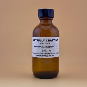 May include: A brown glass bottle with a black cap, labeled "ARTFULLY CRAFTING PINEAPPLE Premium Grade Fragrance Oil." The bottle contains 2 fl oz (59.14 ml) of oil. The label also includes a warning and a website address.
