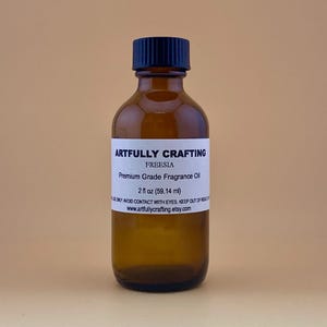 May include: A brown glass bottle with a black cap, labeled "Artfully Crafting Freesia Premium Grade Fragrance Oil 2 fl oz (59.14 ml)".
