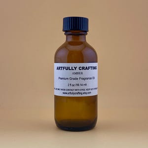 May include: A brown glass bottle with a black cap, labeled "Artfully Crafting Amber Premium Grade Fragrance Oil 2 fl oz (59.14 ml)".