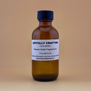 May include: A brown glass bottle with a black cap, labeled "ARTFULLY CRAFTING CRANBERRY Premium Grade Fragrance Oil 2 fl oz (59.14 ml)" and "www.artfullycrafting.etsy.com".