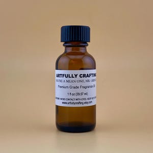 May include: A small amber glass bottle with a black lid. The bottle is labeled "Artfully Crafting" and contains a premium grade fragrance oil. The label also states "You're a Mean One, Mr. Grinch" and "1 fl oz (29.57 ml)".