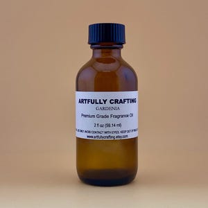 May include: A brown glass bottle with a black cap, labeled "Artfully Crafting Gardenia Premium Grade Fragrance Oil 2 fl oz (59.14 ml)".