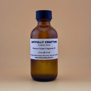 May include: A brown glass bottle with a black cap, labeled "Artfully Crafting Forest Pine Premium Grade Fragrance Oil 2 fl oz (59.14 ml)".