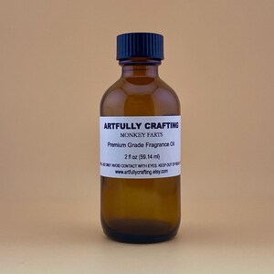 May include: A brown glass bottle with a black cap, labeled "ARTFULLY CRAFTING MONKEY FARTS Premium Grade Fragrance Oil 2 fl oz (59.14 ml)" and "www.artfullycrafting.etsy.com".