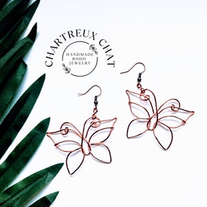 May include: A pair of copper wire butterfly earrings with a delicate, intricate design. The earrings are handmade and feature a simple hook closure.