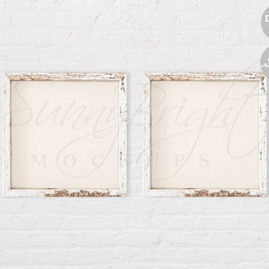 Puede incluir: Dos marcos de fotos cuadrados blancos con bordes desgastados, colgados en una pared de ladrillo blanco. Los marcos están vacíos.