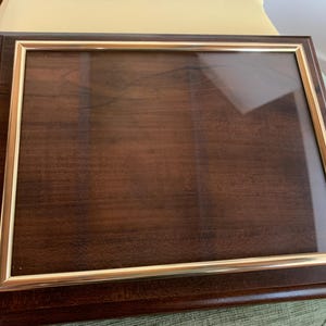 May include: A rectangular wooden display case with a dark brown finish and a clear glass front panel. The glass is framed by a thin, metallic gold-colored border, and the entire structure features a polished, smooth surface with visible wood grain.
