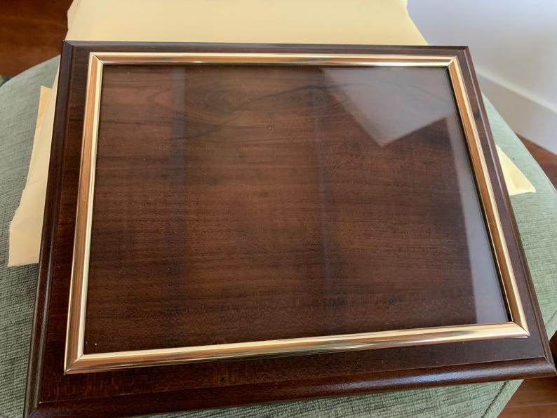 May include: A rectangular wooden display case with a dark brown finish and a clear glass front panel. The glass is framed by a thin, metallic gold-coloured border, and the entire structure features a polished, smooth surface with visible wood grain.
